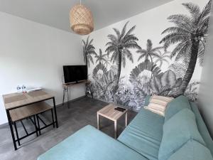 a living room with a blue couch and palm trees mural at La petite maison in Brienon-sur-Armançon