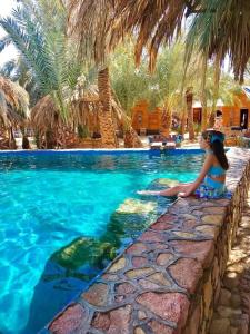 a woman sitting on a wall next to a swimming pool at Marassina camp in Siwa