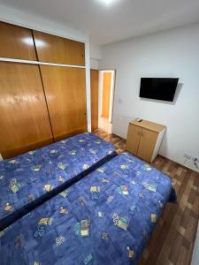 um quarto com uma cama com um edredão azul e uma televisão em Departamento Ciudad Jardín em Billinghurst