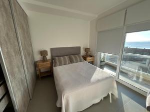 a white bedroom with a bed and a large window at Al Mar in Pinamar +6 photos