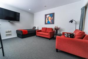 a living room with two red chairs and a flat screen tv at Aubyn Court Spa Motel in Palmerston North