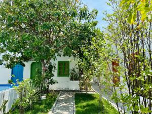a white house with green doors and trees at Moonbeam Homestay & Mini-resort Mui Ne in Phan Thiet