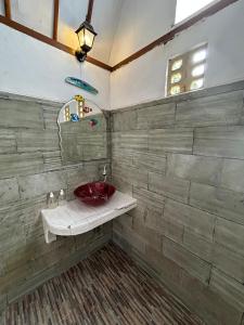 baño con lavabo rojo en una pared de piedra en We'Be Cottages, en Gili Meno