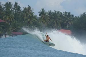 un hombre montando una ola en una tabla de surf en el agua en Nias Falaga Home en Lagudri