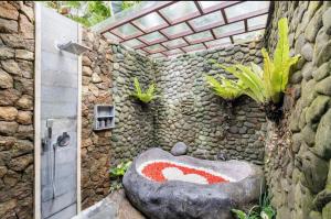 a stone bathroom with a large rock bathtub with plants at Govinda Villas in Penginyahan