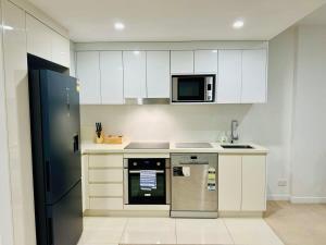 uma cozinha com armários brancos e um frigorífico de aço inoxidável em CASSA TOOWONG - Convenient 1B Apt at Central Location with Parking Managed by The Cassa em Brisbane