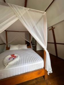 a canopy bed with white sheets and flowers on it at We'Be Cottages in Gili Meno