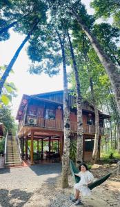 a woman sitting in a hammock in front of a house at Cát Tiên Riverside in Tân Phú