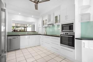 a white kitchen with white cabinets and appliances at Trinity Beach Stunner - Tropical Entertainer in Trinity Beach