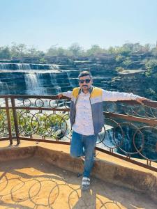 Un hombre de pie junto a una barandilla con una cascada. en Ramaya’s Home Stay, en Varanasi