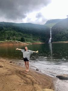 a woman standing on the shore of a lake with a waterfall at Hotel mango tree nearest Adam's peak in Adams Peak