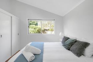 a white bedroom with a bed with a window at Cosy Getaway with Fireplace and Spacious Backyard in Broulee