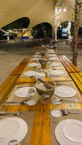 una larga mesa de madera con platos y cuencos blancos en Kawaland glamping resort, en Telukbakau