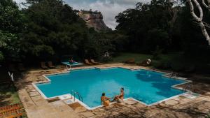two men are sitting in a swimming pool at Sigiriya Village in Sigiriya