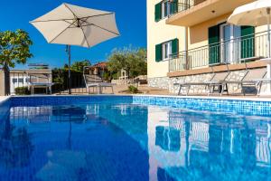 a swimming pool with an umbrella and a house at Apartment Krk David & Matej in Linardići