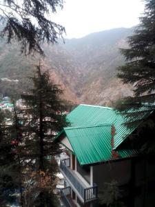 Himalayan Beautiful Mountain View Hostel في دارامشالا: مبنى ذو سقف أخضر مع جبال في الخلفية
