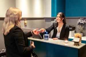 two women shaking hands at a counter in a room at Queen's Hotel by First Hotels in Stockholm
