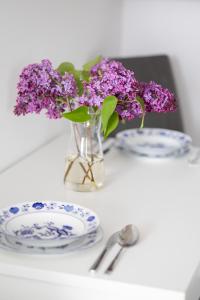 a vase of purple flowers on a table with plates at Bright Studio Głowackiego for 2 People in Warsaw by Renters in Warsaw