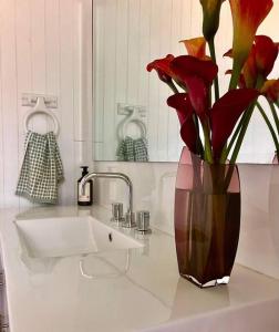 un jarrón con flores rojas sentado en el lavabo del baño en Bruny Serenade, en Adventure Bay