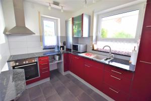 a kitchen with red cabinets and a sink and two windows at Gästehaus Jäger Ferienwohnungen in Gersfeld