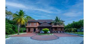 a large brick house with palm trees in front of it at Kumarakom Heritage Resort & Ayurveda in Alleppey
