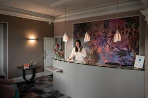 a woman talking on a cell phone behind a counter at The Originals Boutique, Hôtel Normandie, Auxerre in Auxerre