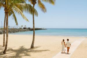una pareja de pie en una playa con palmeras en Arrecife Gran Hotel & Spa, en Arrecife