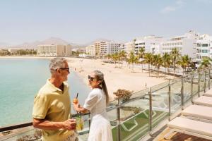 an older man and woman standing on a balcony overlooking a beach at Arrecife Gran Hotel & Spa in Arrecife