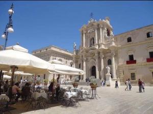 un grand bâtiment avec des tables et des parasols dans une cour dans l'établissement Casetta del Borgo, à Syracuse