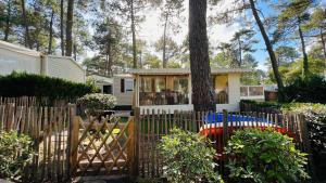 a fence with a tree in front of a house at Mobilhome climatisé, 6 personnes camping les embruns in Lège-Cap-Ferret