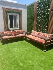 two benches sitting on a patio with green grass at شاليهات الرويلي in Al Fayşalīyah