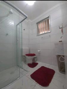 a bathroom with a shower and a toilet with red rugs at Apartamento na Praia in Praia Grande