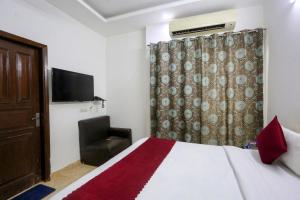 Hotel Shillo Nizamuddin في نيودلهي: غرفة نوم بسرير وكرسي وتلفزيون