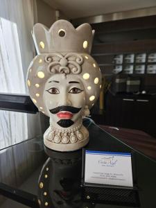 a statue of a mask on a glass table with a sign at Hotel Costa Azul in Balestrate