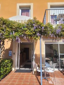 un patio con mesa, sillas y flores púrpuras en Hôtel de l'Orb, en Bédarieux