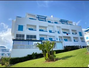 a white building with blue windows on top of a green field at Appartement prestigieux à Smir Park M'diq in Marina Smir