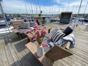 a wooden deck with couches and a table with flowers at Hausboot Yara am Steg 1D in Heiligenhafen