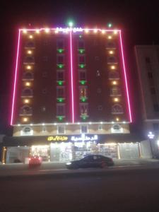 Quwayzah的住宿－كيان التيسير للشقق المخدومة - Kayan Al Tayseer Serviced Apartments，一座大型建筑,上面有粉红色和绿色的灯光