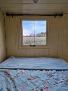 a bed in a small room with a window at Delilah the shepherd's hut in Sidlesham