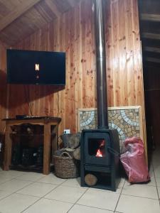 a woodburning stove in a room with a tv at Cabaña Beatriz in Coñaripe