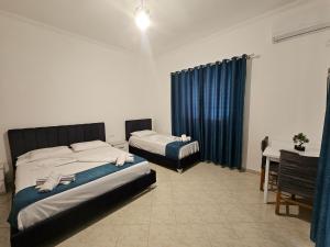 two beds in a room with blue curtains and a table at DEA Room 1 in Sarandë
