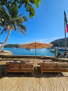 two benches with an umbrella on a beach at Pousada e Mergulho Jamanta in Angra dos Reis