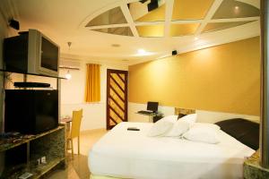 Vert Motel Parnamirim في بارناميريم: غرفة نوم مع سرير أبيض وتلفزيون على الحائط