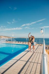 a couple standing next to a swimming pool on a cruise ship at Gillieru Harbour Hotel in St. Paul's Bay