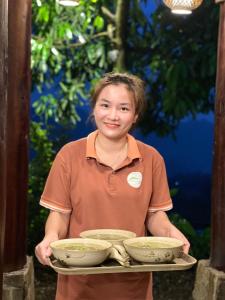 un joven sosteniendo una bandeja con tres tazones en Pu Luong Paradise en Hương Bá Thước