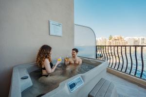 Un uomo e una donna seduti in una vasca da bagno di Gillieru Harbour Hotel a San Pawl il-Baħar
