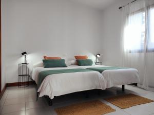 Un dormitorio blanco con una cama grande con almohadas verdes y naranjas. en Casa María, en Tías