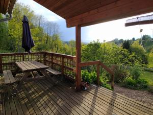 eine Holzterrasse mit einem Picknicktisch und einem Sonnenschirm in der Unterkunft Room with en suite bathroom in cosy wooden house in Rimont