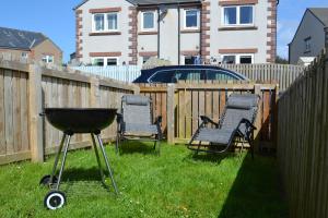 a grill and chairs in a backyard with a fence at Normsy Place Seaside Serenity Breath Taking Views in St Bees