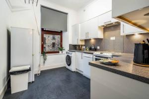 cocina con armarios blancos, lavadora y secadora en Caledonia Suite - Netflix Free Parking en Glasgow